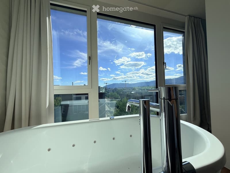 Modern bathroom with a large bathtub, sleek chrome faucet, and large windows offering a scenic view of the city and mountains.