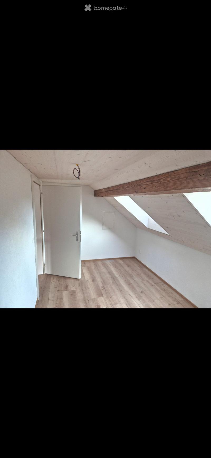 Empty attic room with wooden floor, white walls, exposed wooden beams, and skylight windows.