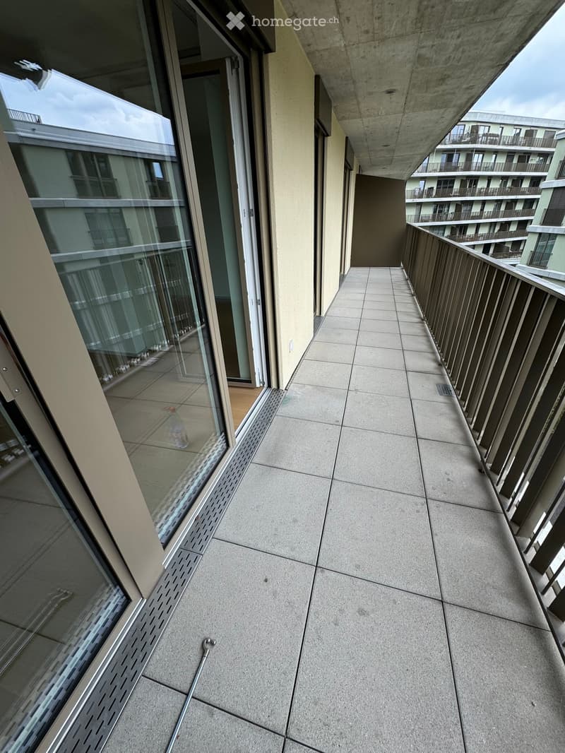 Modern balcony with tiled floor, glass railing, and view of neighboring buildings.