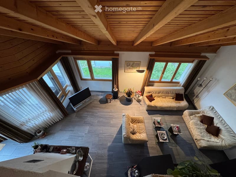 A modern living room with a high wooden ceiling, large windows, and multiple seating areas including sofas and a coffee table.