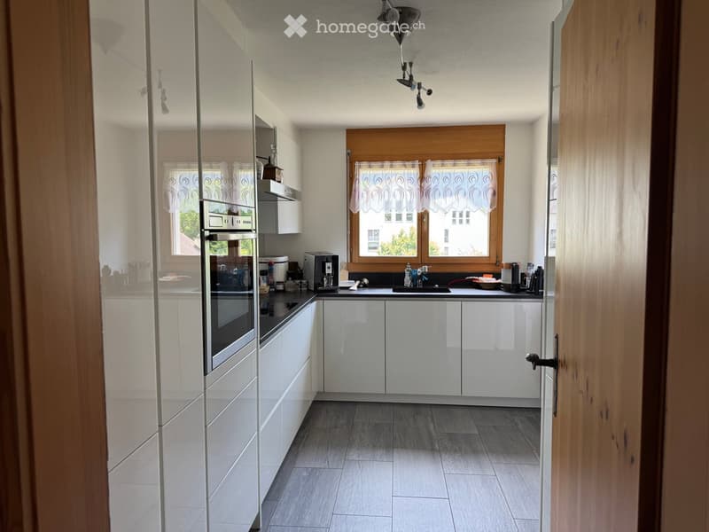 Modern kitchen with white cabinets, stainless steel oven, central island, and large windows with curtains.