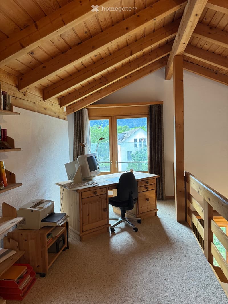 Cozy attic study with wooden beams, large windows, desk, chair, computer, printer, and shelves with books.
