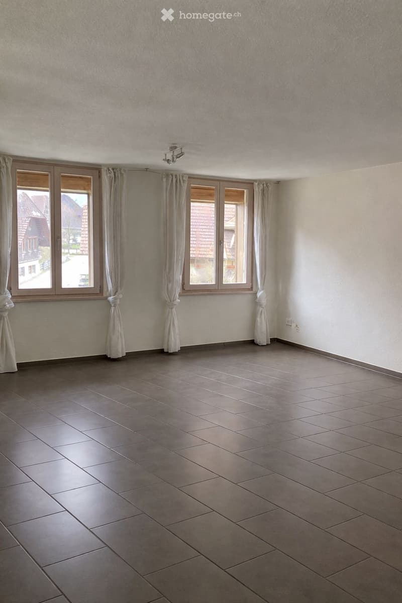 Empty room with tiled floor, large windows with curtains, and a ceiling light fixture.