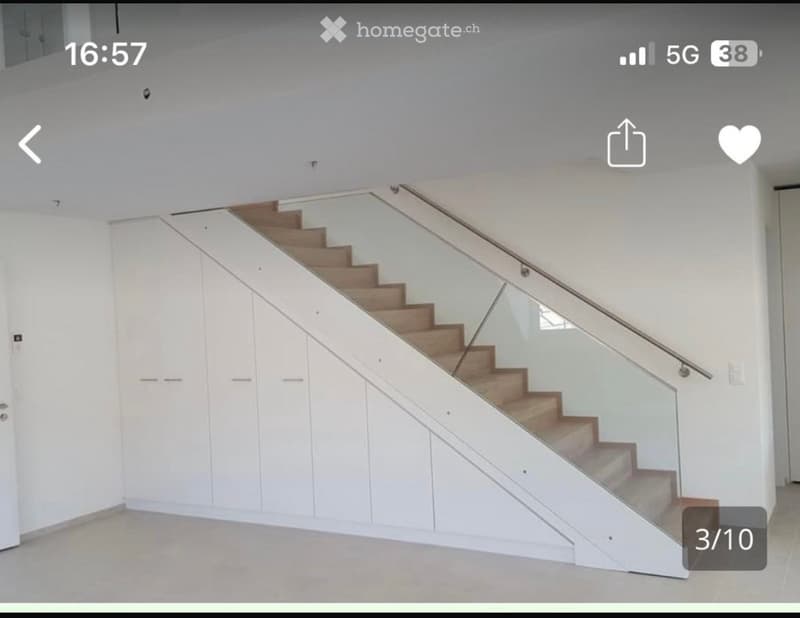 Modern staircase with wooden steps and glass railing, white built-in storage cabinets on one side, light-colored walls and floor.