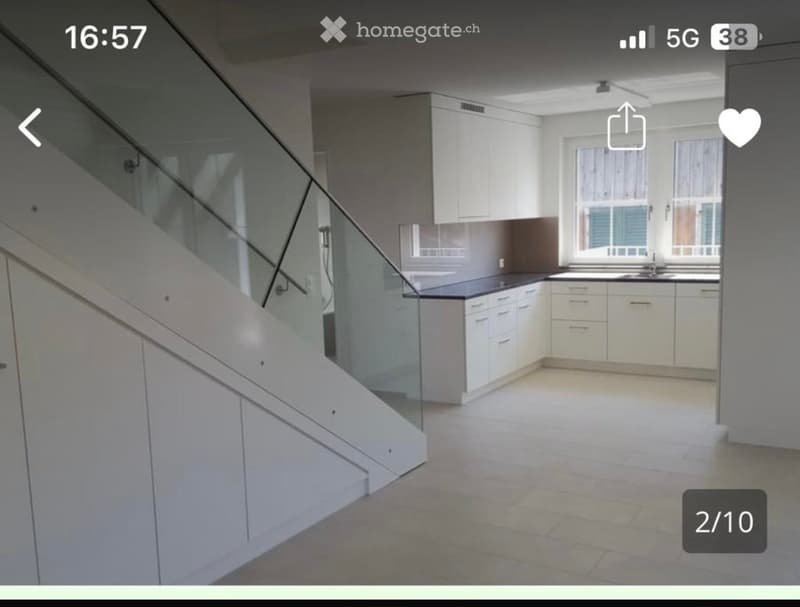 Empty kitchen with white cabinets, black countertops, and a staircase with a glass railing leading upwards.