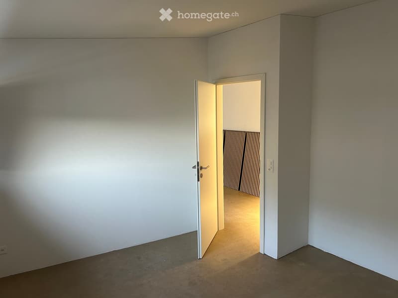 Empty room with white walls, carpeted floor, and an open door leading to another room with striped curtains.
