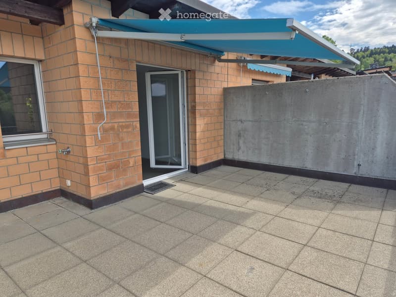 Balcony with tiled floor, brick wall, sliding glass door, and retractable awning.