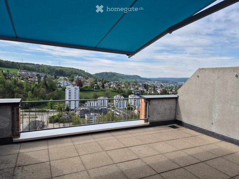 Balcony with tiled floor, metal railing, and a retractable awning, offering a panoramic view of a cityscape and surrounding greenery.