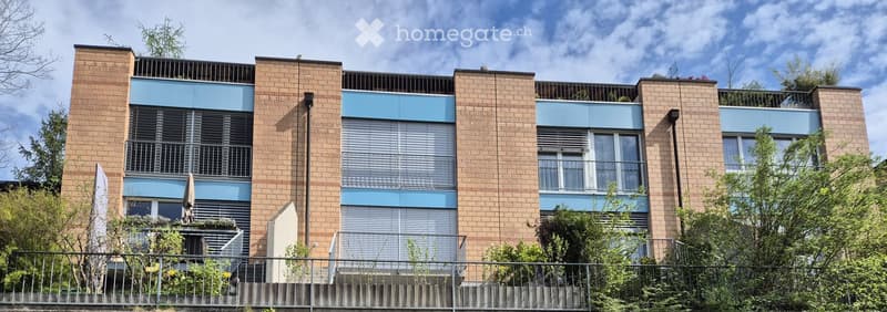 Modern multi-story apartment building with brick facade and blue accents, featuring balconies and large windows.