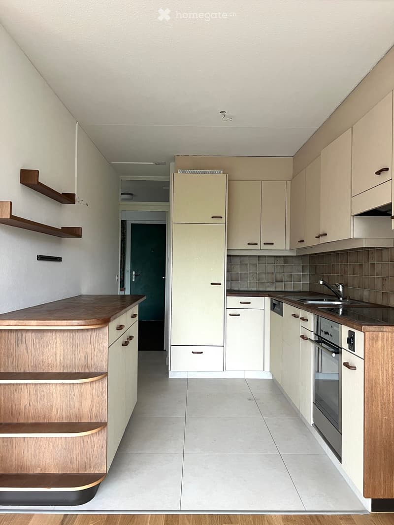 Modern kitchen with light-colored cabinets, wooden countertop, sink, and built-in oven. The space features tiled backsplash and open shelving.