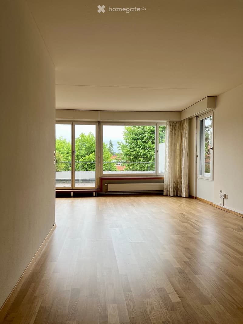 Empty room with wooden flooring, large windows, and a radiator. No furniture or equipment present.