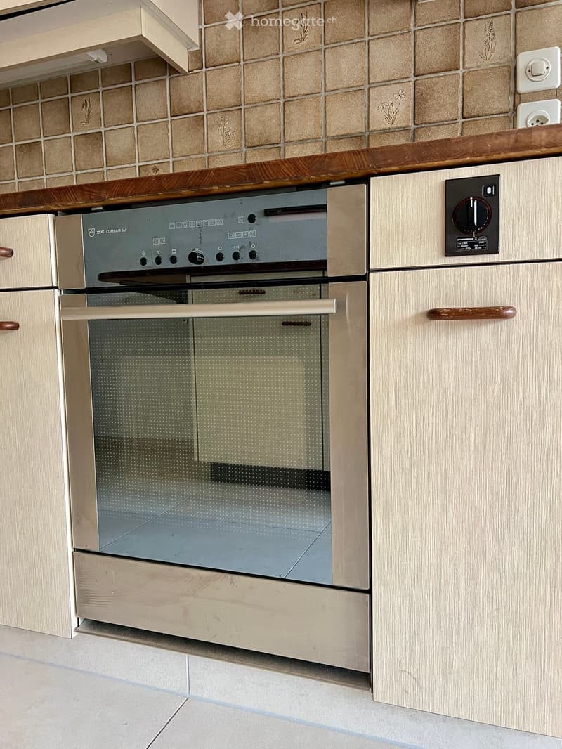 Modern kitchen with light wood cabinets, stainless steel oven, and tiled backsplash.