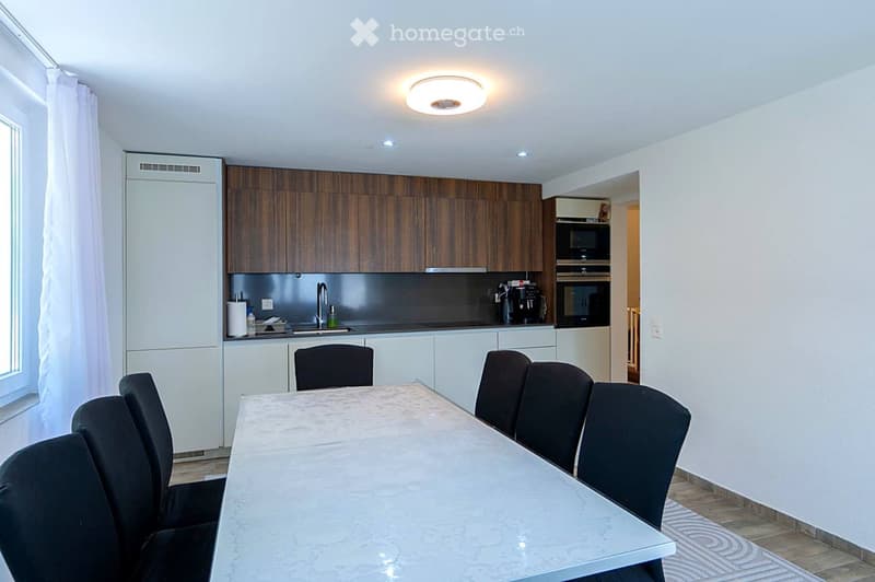 Modern kitchen with wooden cabinets, stainless steel appliances, a dining table with chairs, and a sleek countertop.