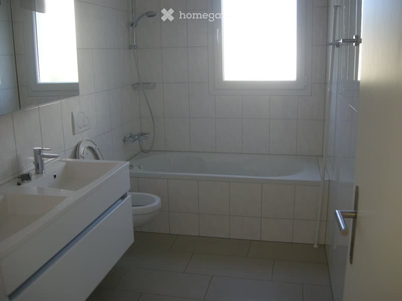 Modern bathroom with white tiles, double sink, bathtub, toilet, and showerhead.