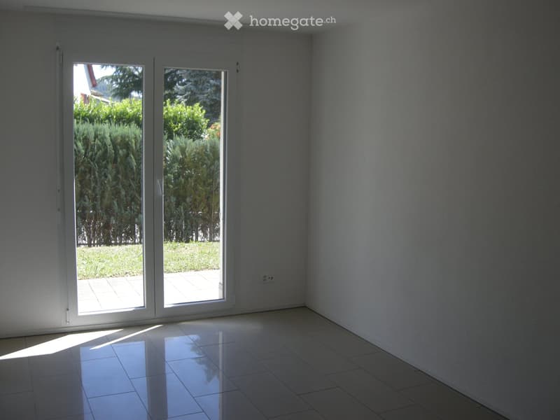 Empty room with white tiled flooring and large sliding glass doors leading to a garden area.