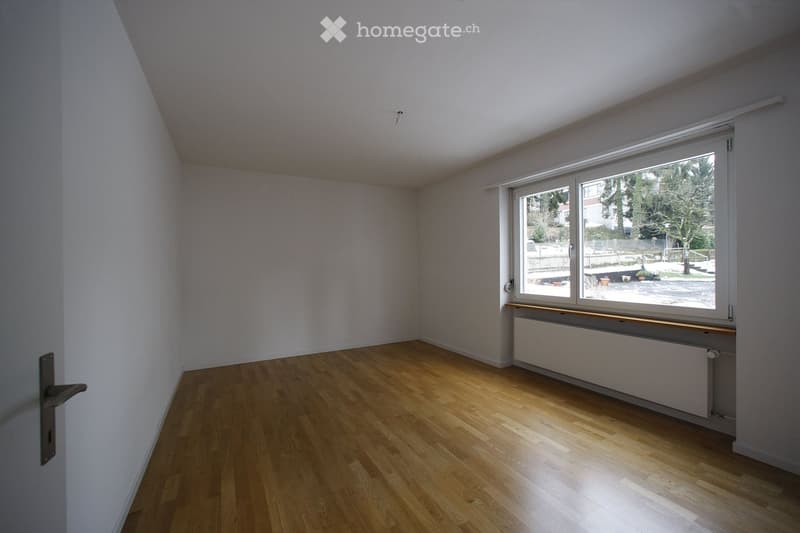 Empty room with wooden flooring, white walls, and a large window with a view of the outdoors.