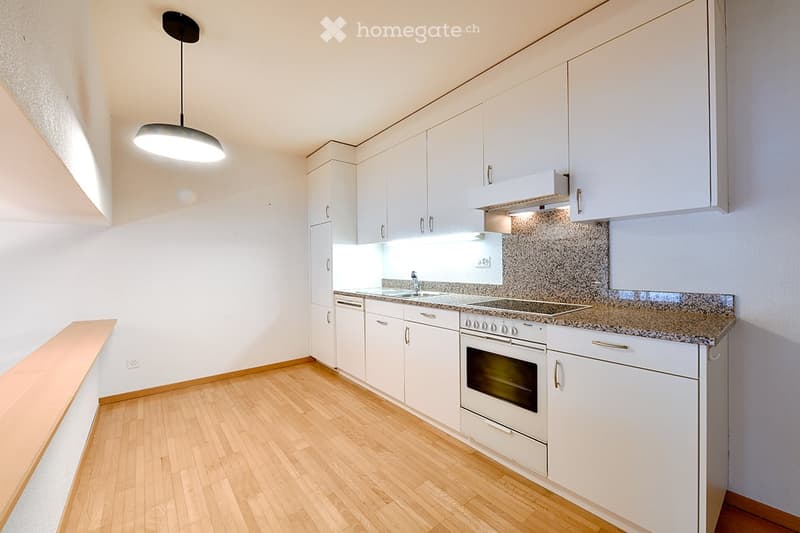 Modern kitchen with wooden floor, white cabinets, marble countertop, white appliances, and a ceiling lamp.