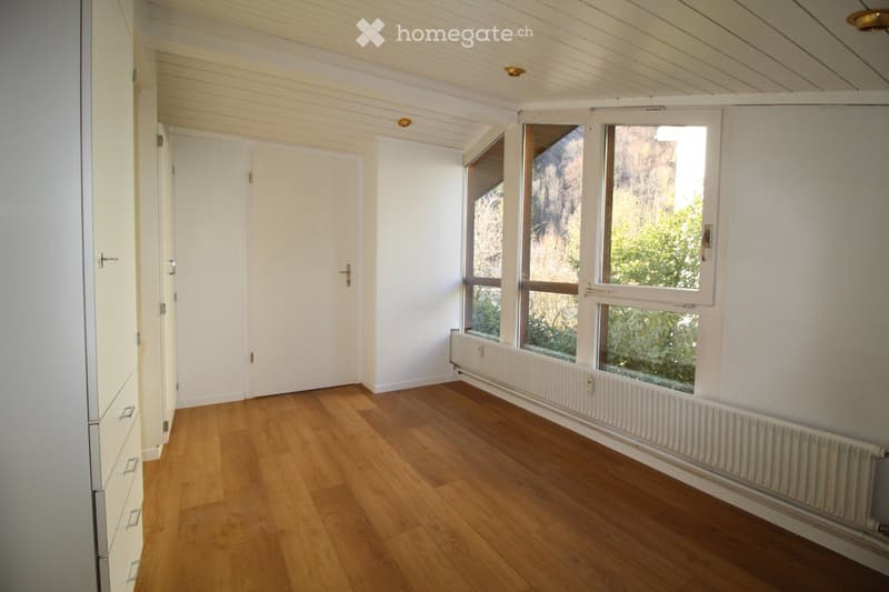 Empty room with wooden flooring, white walls, large windows, and a radiator. No furniture or equipment present.