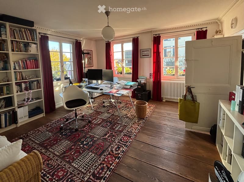 Office room with carpet, desk, office chair, shelves, radiator, bookshelves, picture frames, radiator