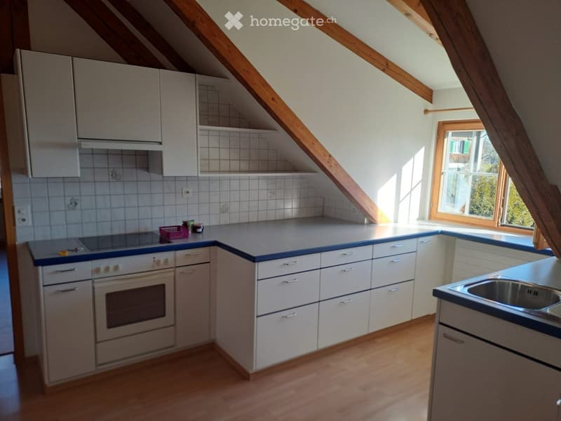 Bright kitchen with white cabinets, wooden floor, and a window letting in natural light. Features an oven, sink, and countertop with a few small items.