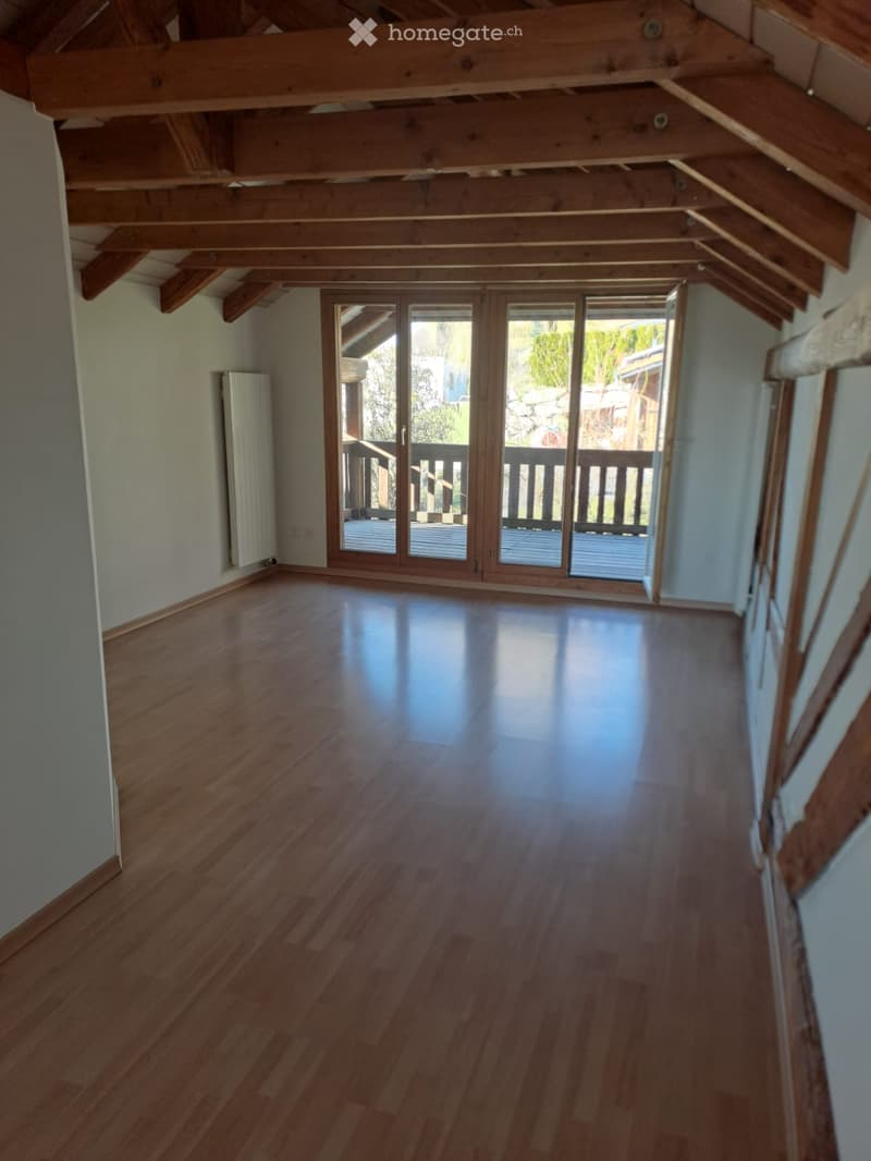 Empty room with wooden flooring, exposed wooden beams on the ceiling, and large sliding glass doors leading to a balcony.