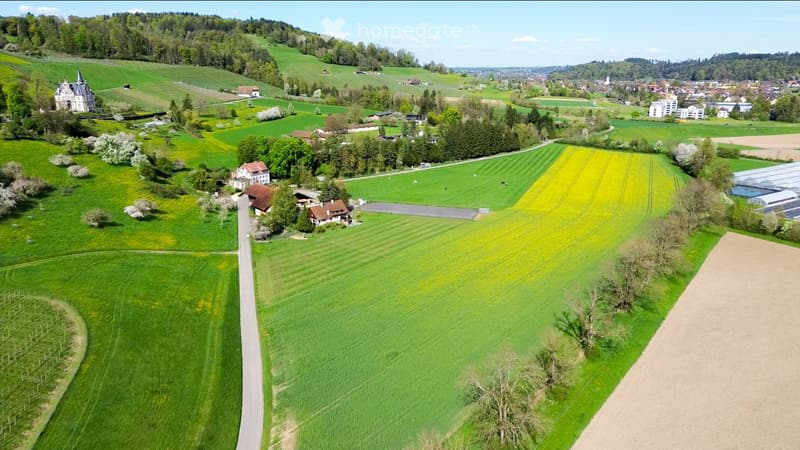 Aerial view of a rural landscape with green fields, scattered houses, and a small town in the distance.
