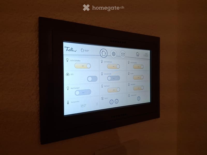 Wall-mounted smart home control panel with touchscreen interface displaying lighting controls and temperature settings.