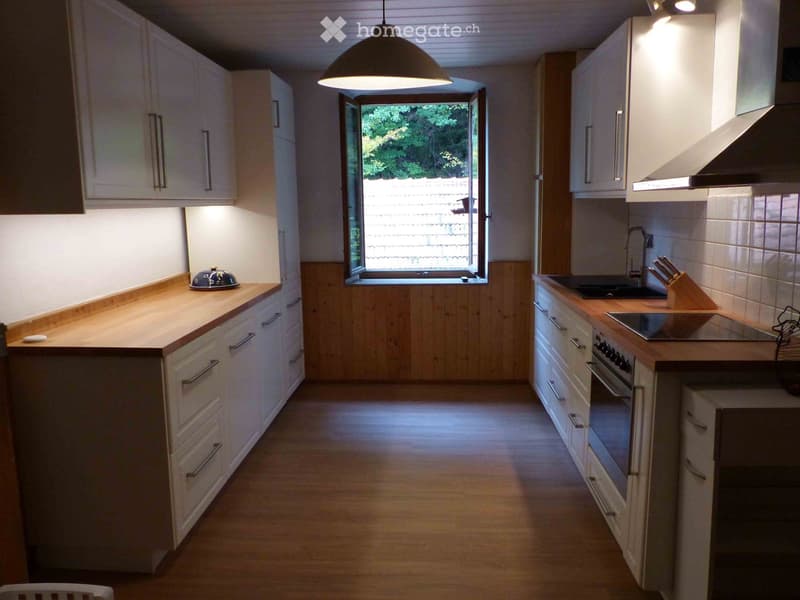 Modern kitchen with white cabinets, wooden countertops, and stainless steel appliances. Features an island with a bowl on the counter and a window overlooking a garden.