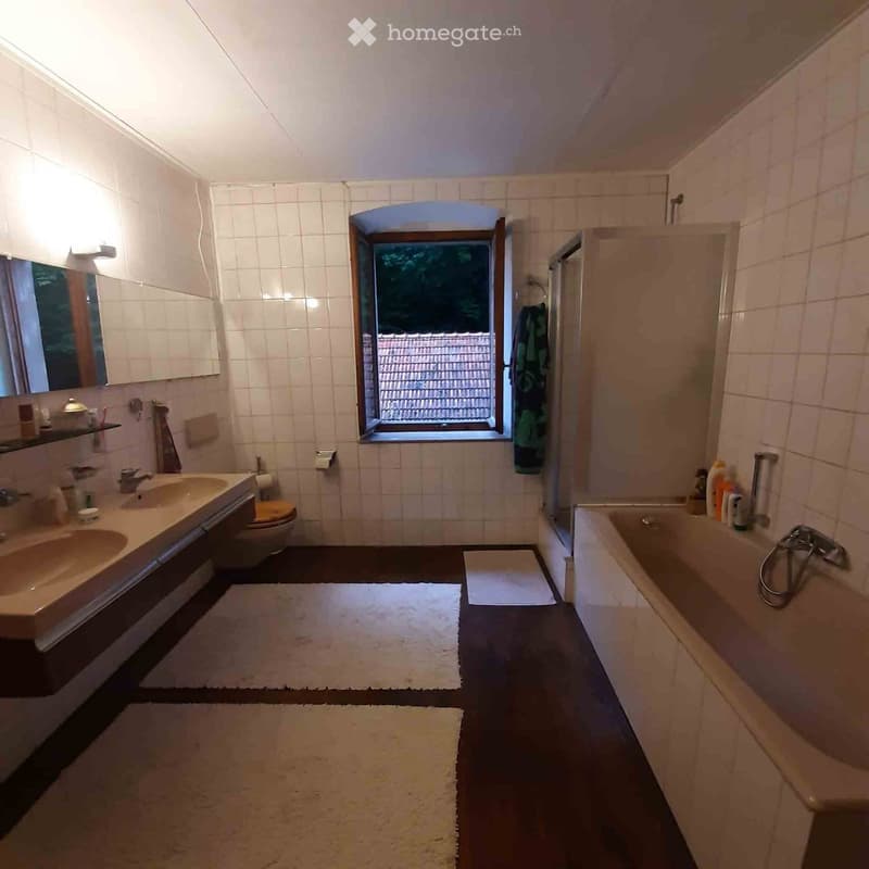 Bathroom with white tiled walls, a sink, toilet, bathtub, mirror, and a window with a view of the outside.