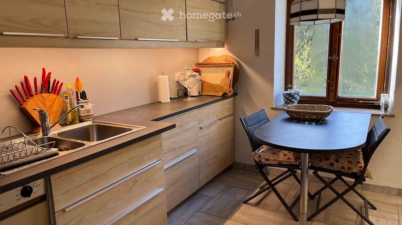 Modern kitchen with wooden cabinets, stainless steel sink, built-in oven, and a small dining area with a table and chairs.