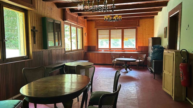 A rustic dining area with wooden walls, large windows, and several tables and chairs arranged for seating.