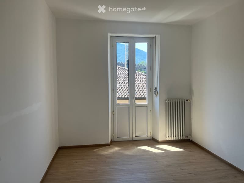 Empty room with wooden flooring, white walls, a double door with glass panels, and a radiator on the right side.