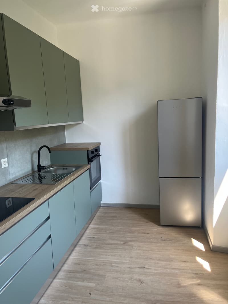 Modern kitchen with light green cabinets, wooden countertops, stainless steel sink, faucet, oven, and refrigerator.