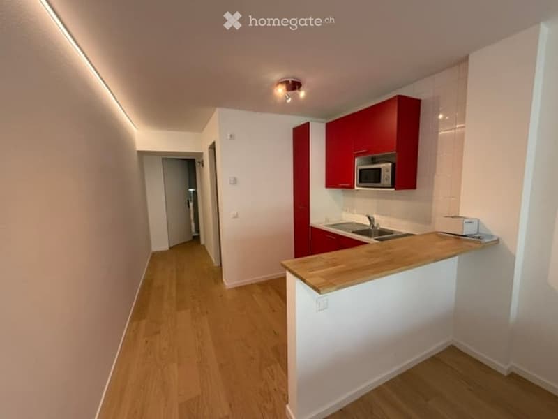 Modern kitchen with red cabinets, a wooden countertop, a microwave, and a sink. The floor is light wood, and the walls are white.