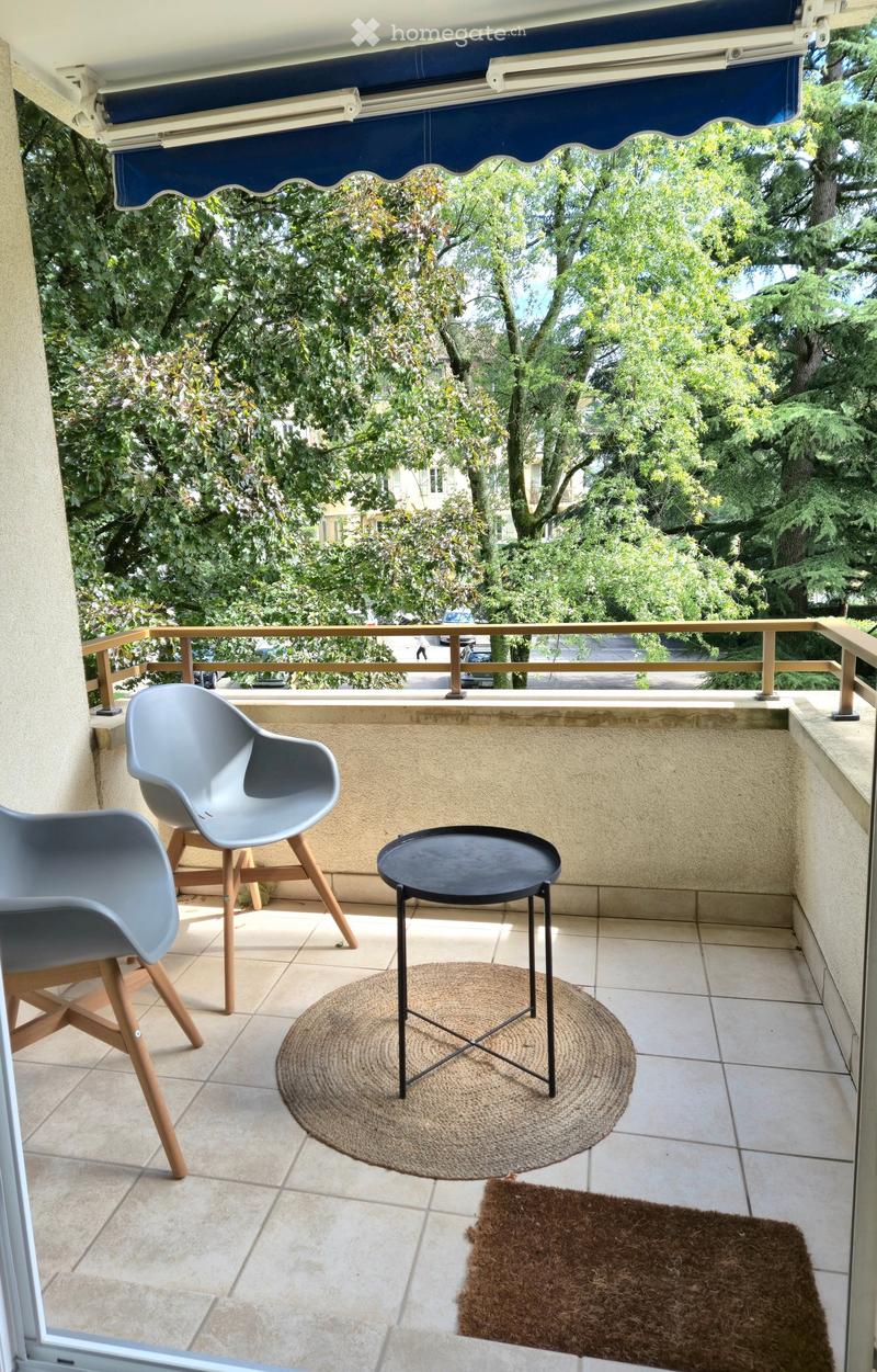 Balcony with tiled floor, two modern chairs, a small black table, and two rugs.