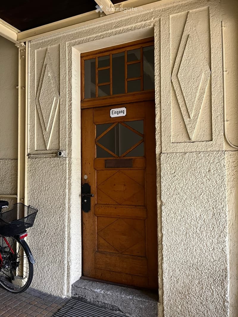 Wooden door with glass panel, label 'Eingang', gray stone wall, mailbox, bicycle parked on left