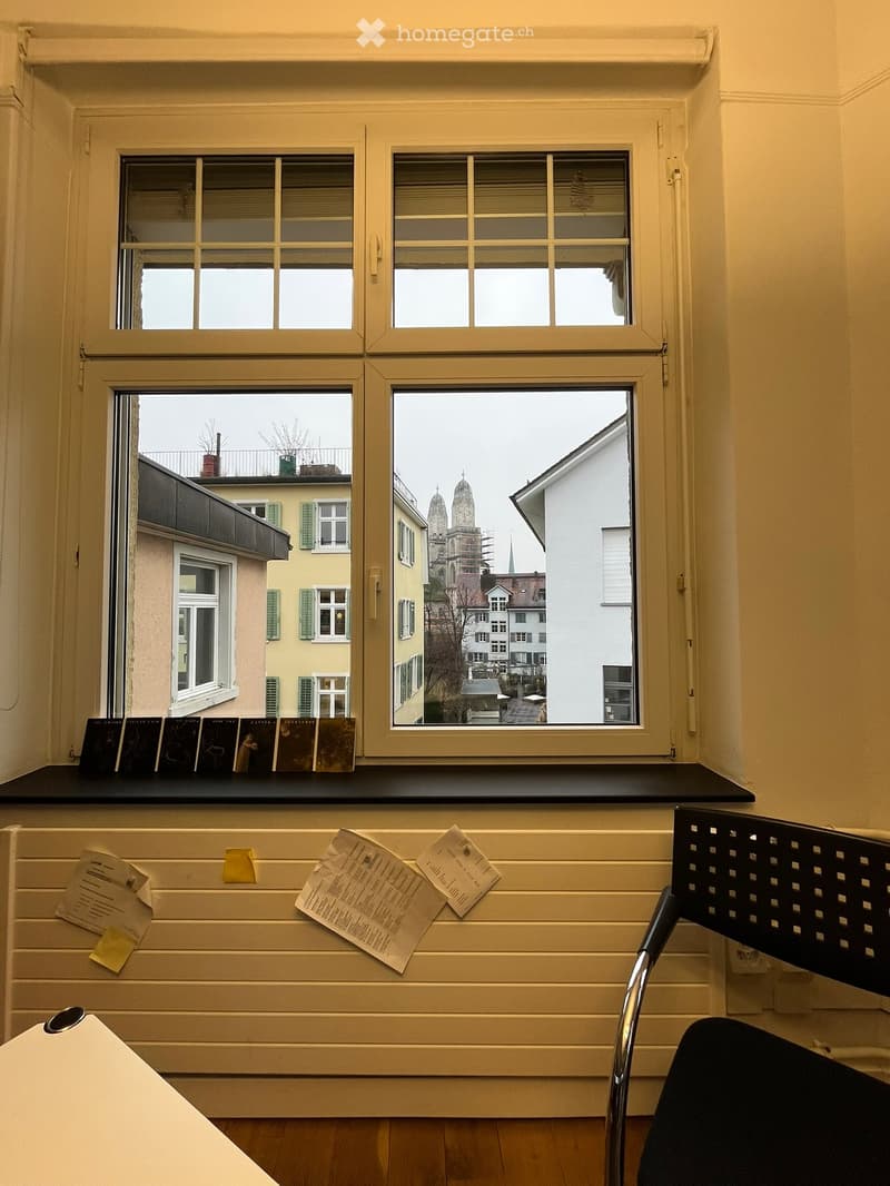 Window with cityscape view, white radiator, black chair, papers attached on radiator