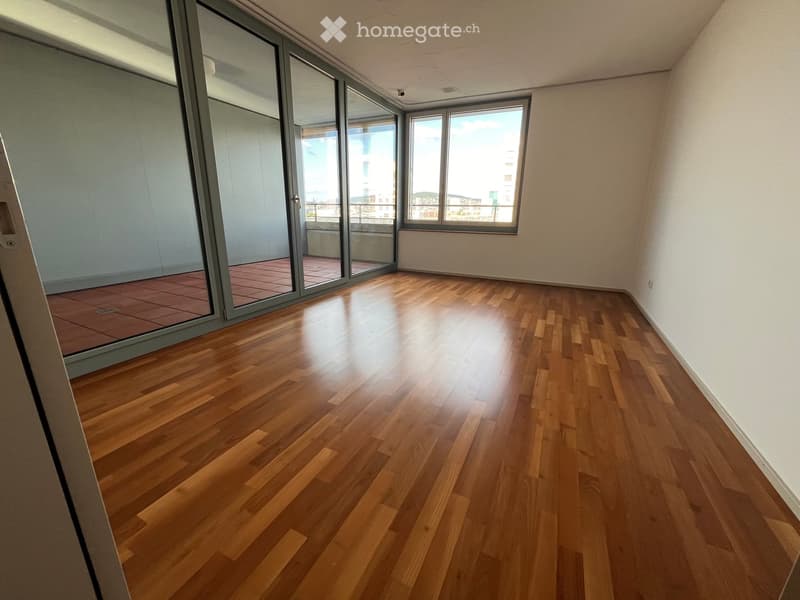 Empty room with wooden flooring, large windows, and sliding glass doors leading to a balcony.