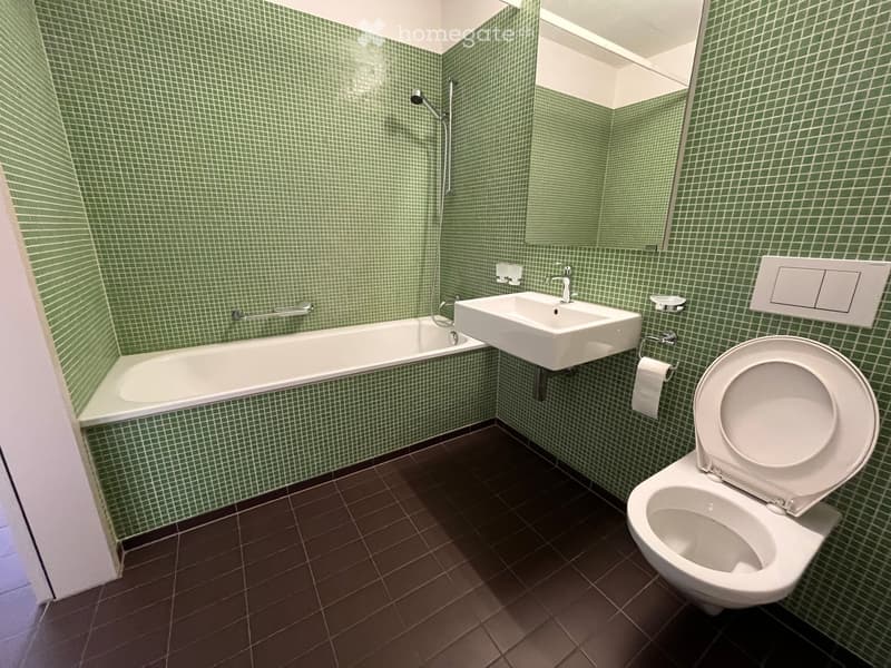 Bathroom with green tiled walls, bathtub, sink, toilet, and a mirror above the sink.