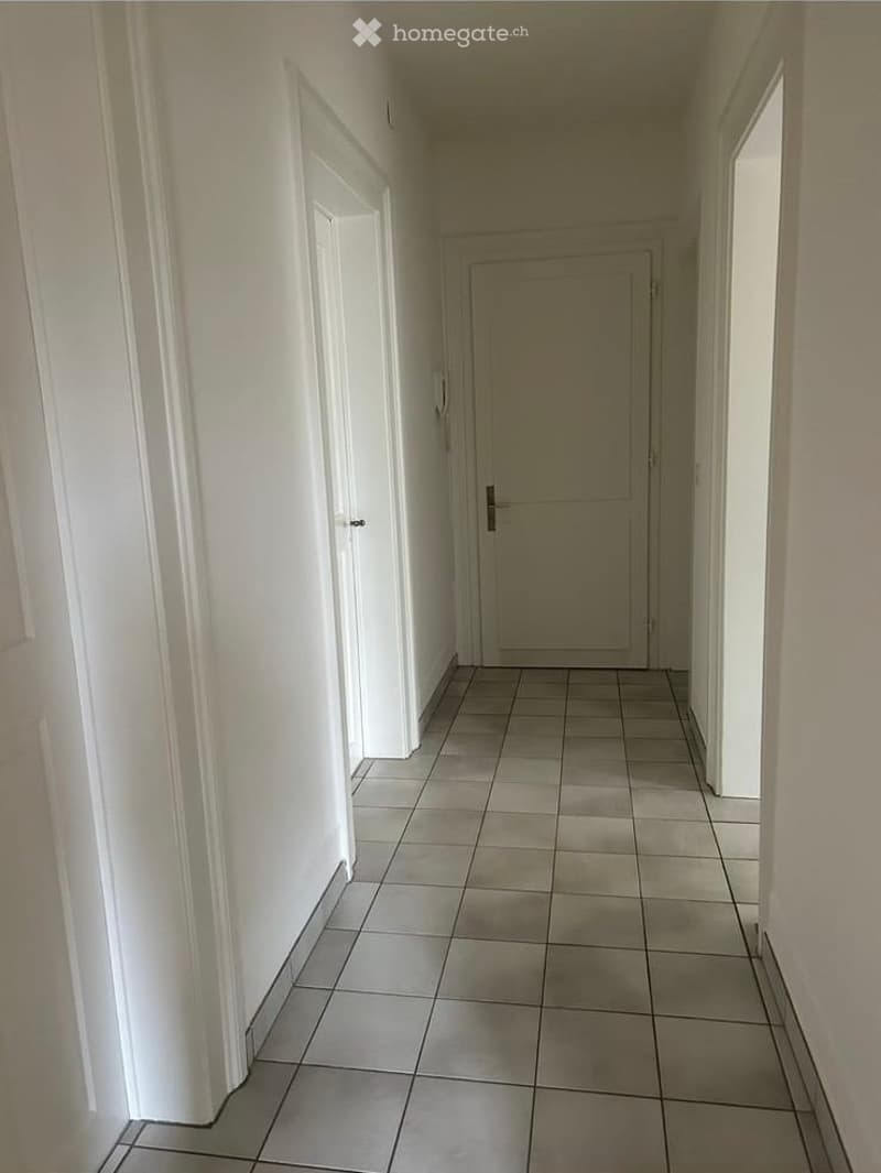 Empty hallway with tiled floor and white walls, featuring closed doors on both sides.