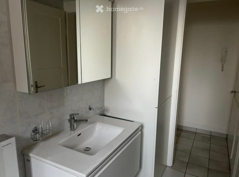 Modern bathroom with a white sink, chrome faucet, mirrored cabinet, and tiled walls.