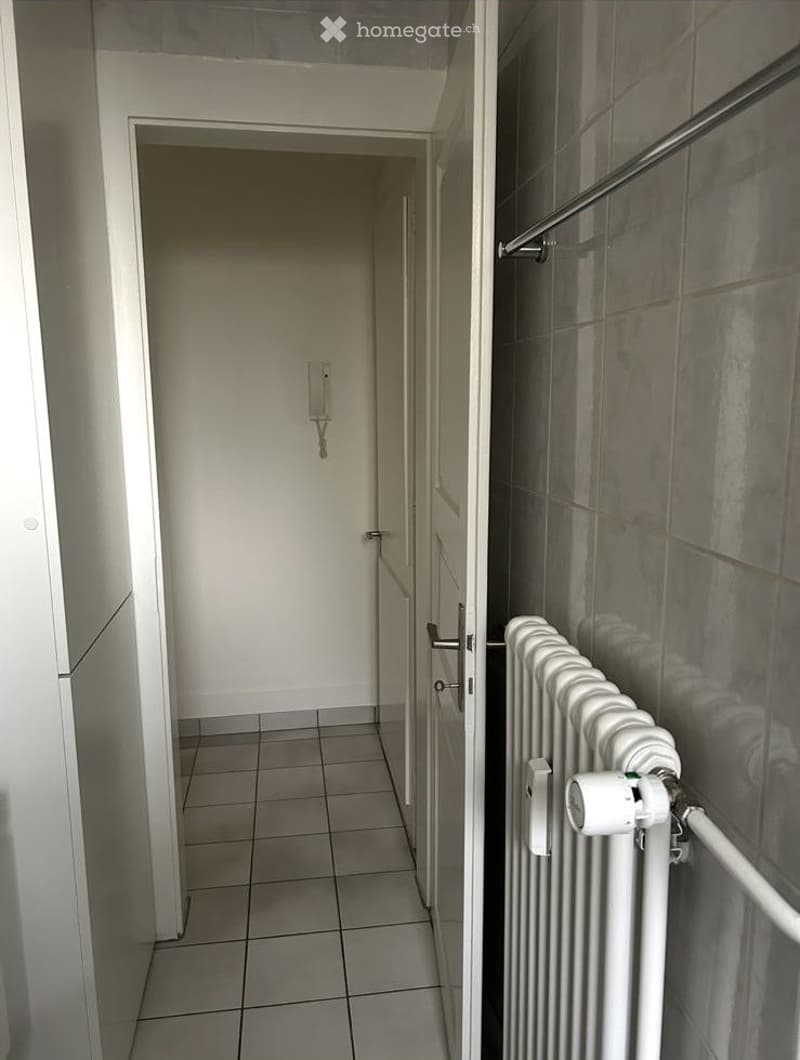 Empty hallway with tiled floor, white walls, and a radiator on the right side.
