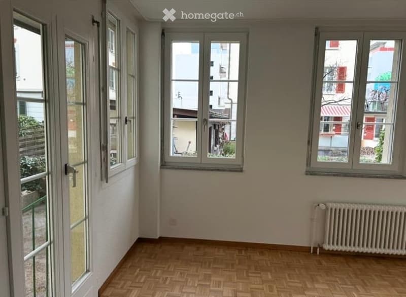 Empty room with wooden flooring, large windows, and a radiator on the wall.