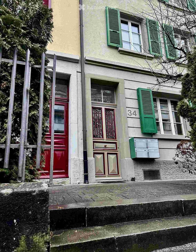 Two-story residential building with green shutters, red doors, and a small staircase leading to the entrance.