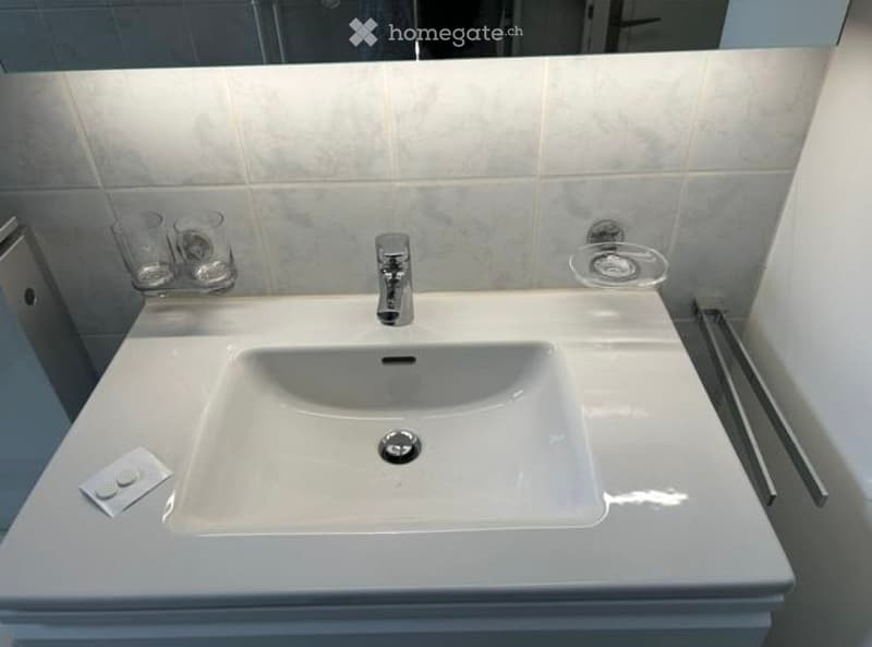 Modern bathroom with a white sink, chrome faucet, toothbrush holder, and a towel rack. The sink has a sleek, contemporary design with a built-in soap dispenser.