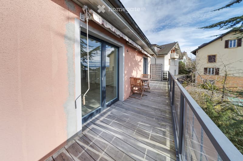 Balcony with wooden decking, glass sliding door, small table and chairs, railing, and view of neighboring houses.