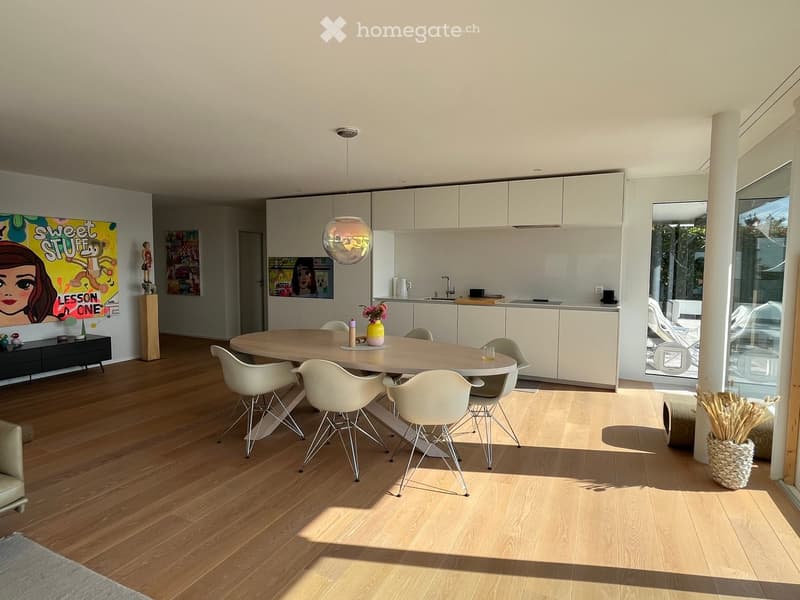 Dining area with wooden floor, round table, white chairs, white cabinets, artwork, pendant light, glass door