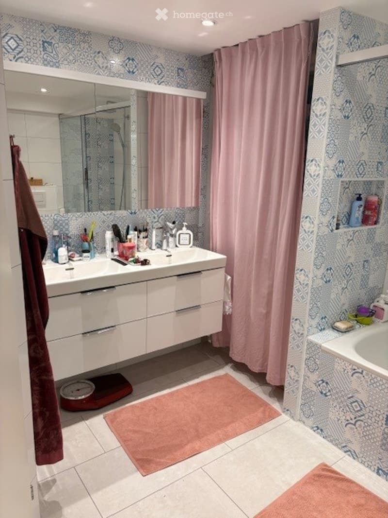 Modern bathroom with white cabinetry, a large mirror, a pink shower curtain, and a bathtub. The floor is tiled, and there are decorative towels and a bathroom scale visible.