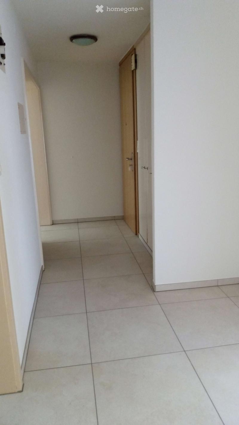 Empty hallway with tiled floor, white walls, and a wooden door on the right side.