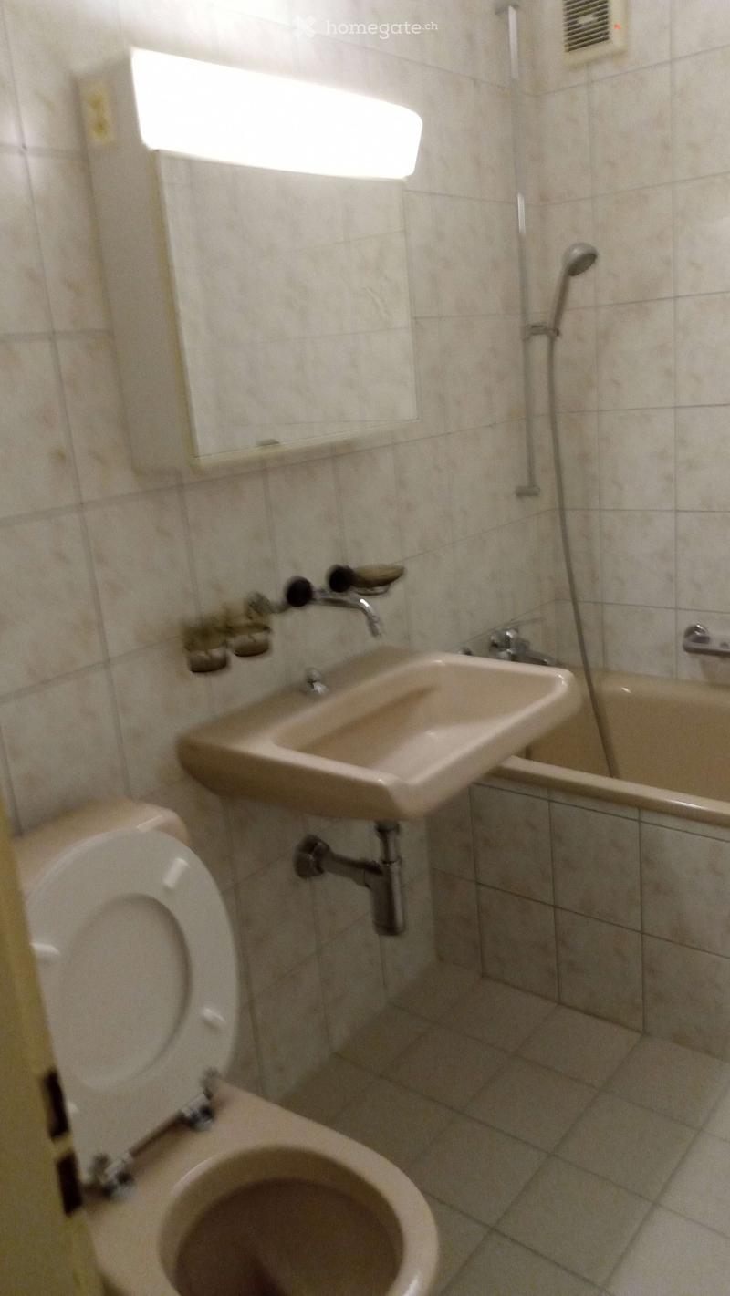Bathroom with beige tiles, a toilet, a sink, a bathtub, a mirror, and a showerhead.